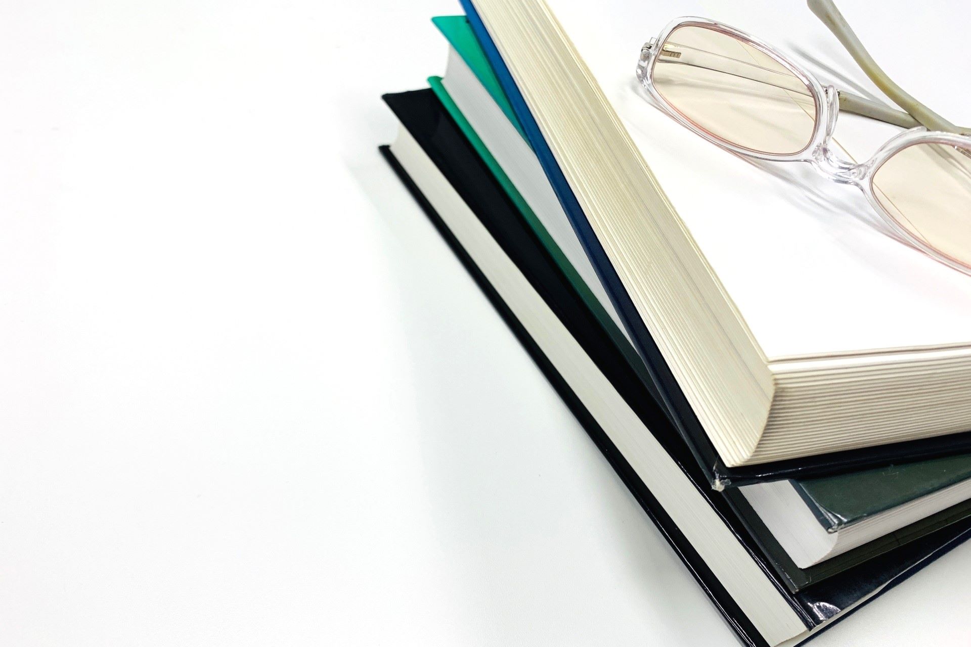 白い背景に積み重ねられた本と透明フレームの読書用めがね