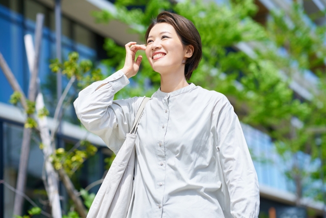 青空の下で白いシャツを着て笑顔で頬に手をあてる人物の横顔