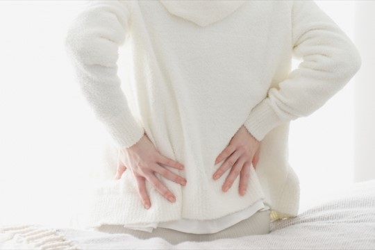 白いセーターを着た人が腰に両手を当てて腰痛のポーズをとっている様子