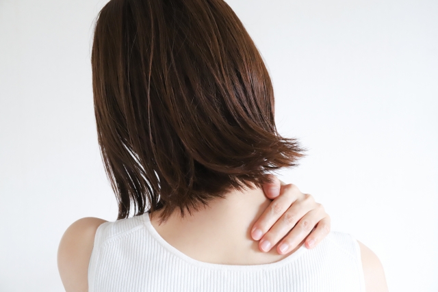 白いタンクトップを着た人が首や肩の痛みに手を当てている様子
