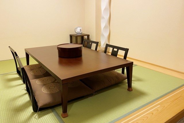 和室に置かれた茶色い座卓と座布団4点 畳の上にサイドテーブルと花瓶も配置